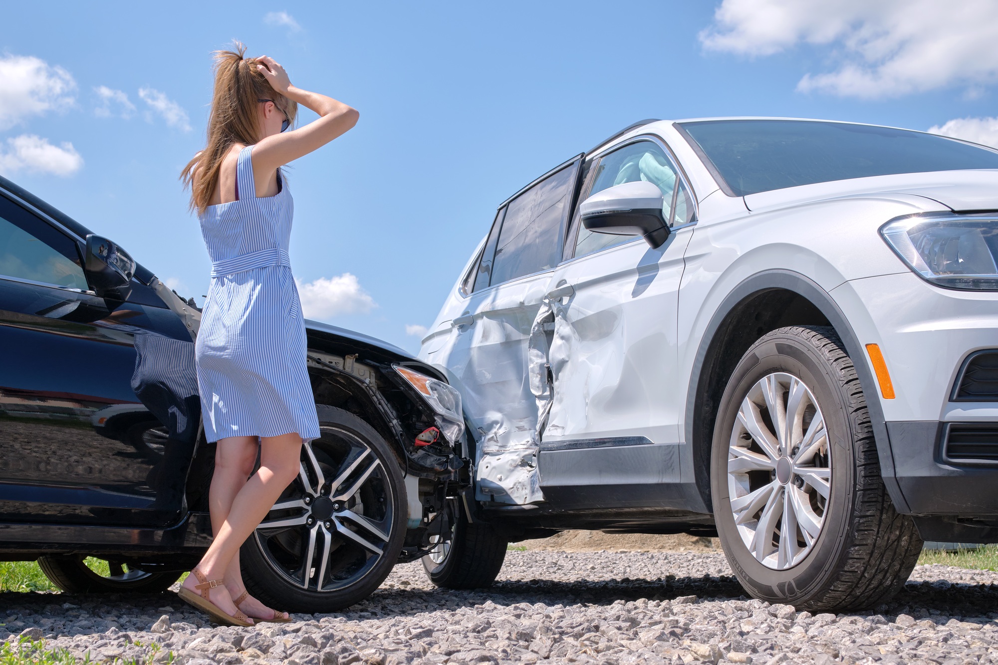 Sad young woman driver standing near her smashed car looking shocked on crashed vehicles in road